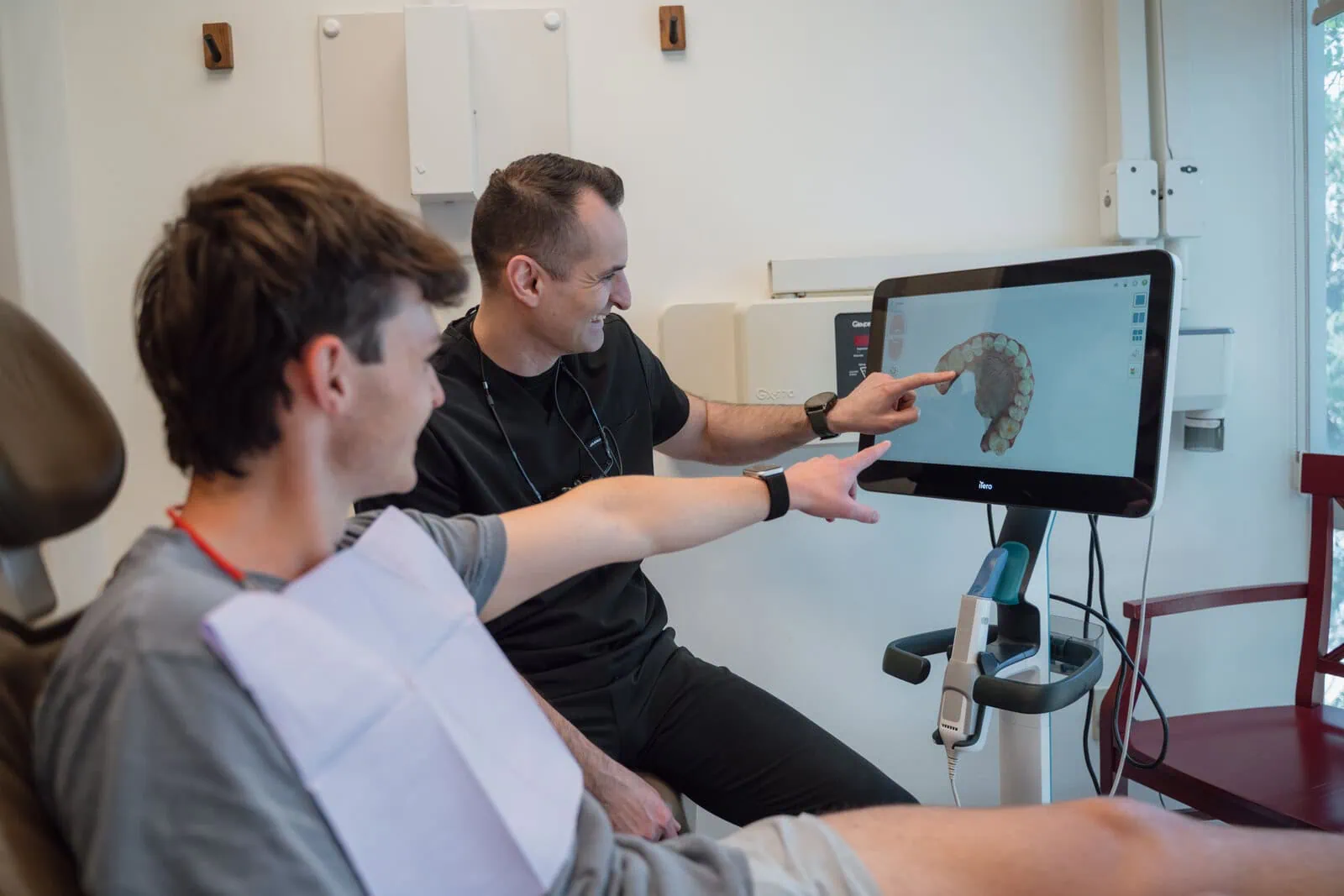 Dentist and patient pointing at a 3D dental model displayed on a computer screen in a dental office.