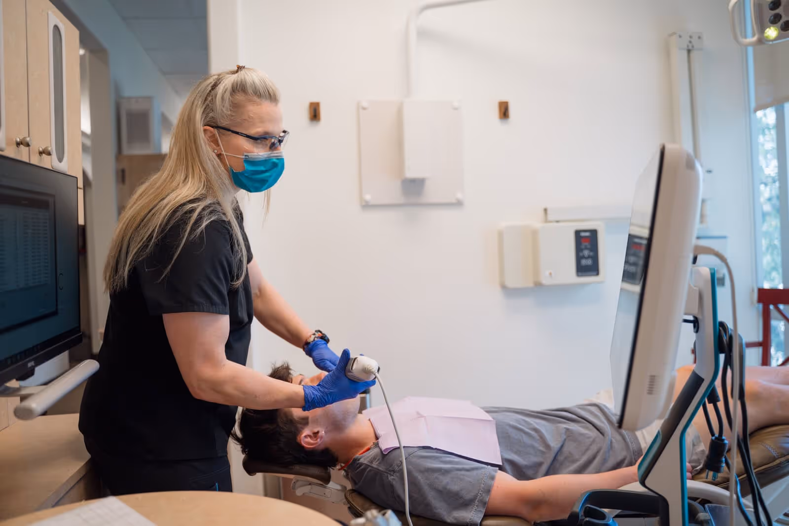 Dental professional wearing mask and gloves using an intraoral scanner on a patient lying in a dental chair.